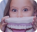 girl having fun playing with a giant set of teeth at the dentist